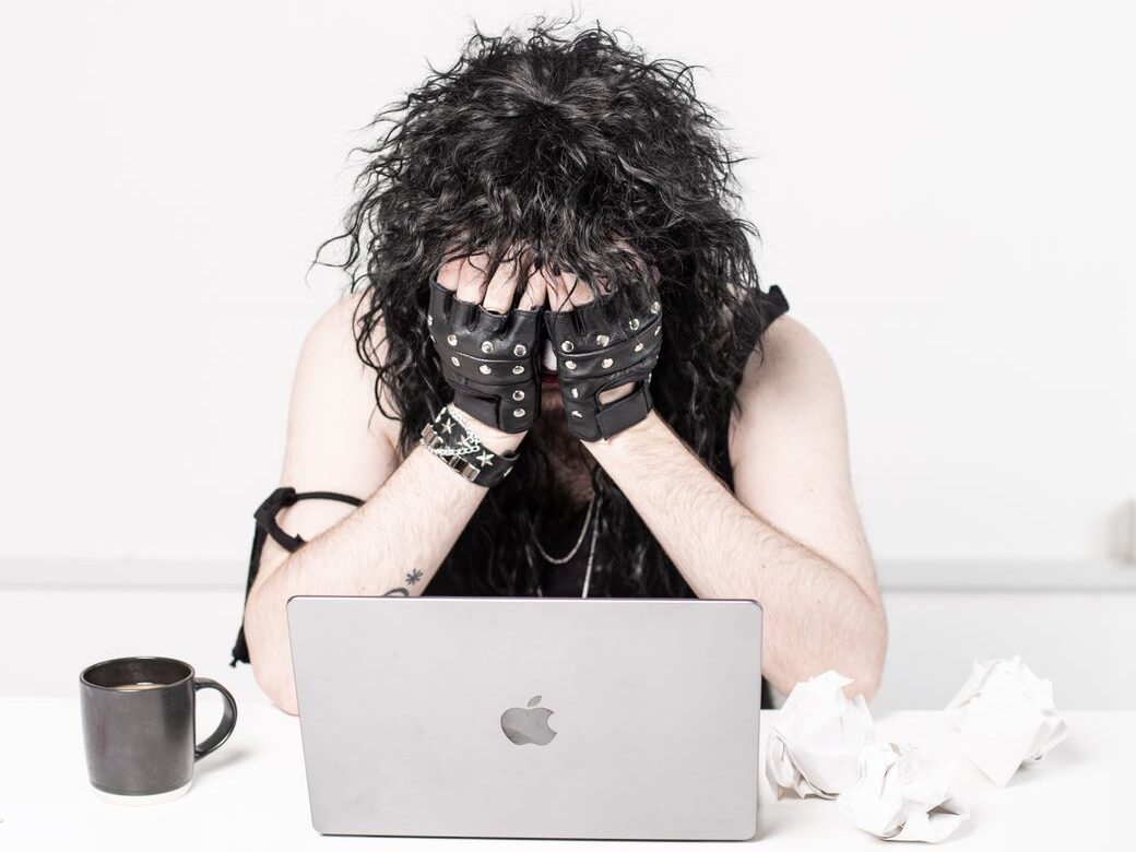 man in gloves sitting with hands on face over laptop