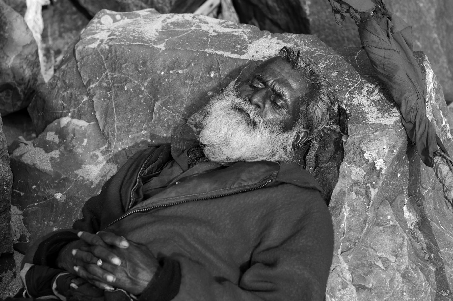 grayscale photo of elderly man sleeping on a rock
