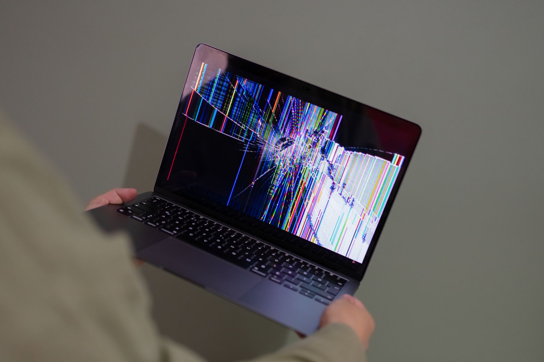 a person holding up a laptop with a broken screen